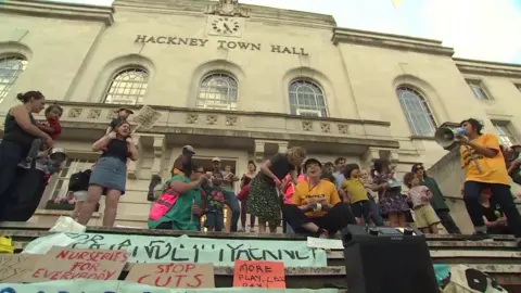 A group of protesters outside Hackney Town Hall to protest against the cuts, there are banners that say "stop cuts" and "nurseries for everybody"