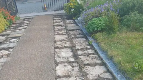 James Fish A mid-shot of the pavement approaching the church. The stones have been torn up.