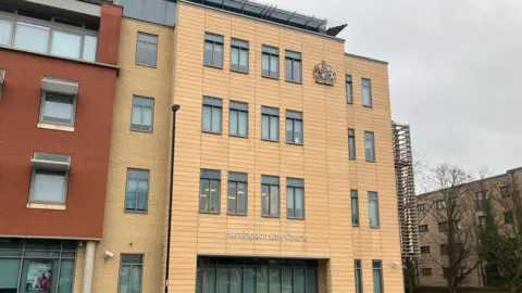 Shariqua Ahmed/BBC Exterior of the crown court building - a yellowing tall building with glass windows.