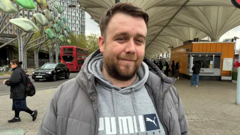 A man in a grey jumper and coat. He had a beard and brown hair.
