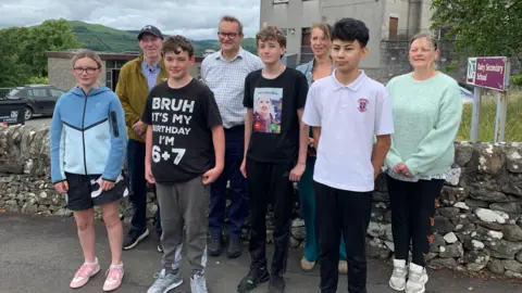 A group of four children and four adults stand in front of Dalry Secondary