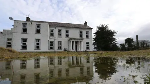 Getty Images The former Marianvale Mother and Baby home in Newry. A dilapidated two-storey building surrounded by overgrown grounds and a holy cross plinth.