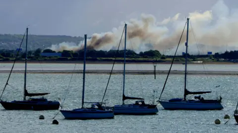 Alison Treacher Smoke from the fire billowing across the sky, with sailboats in he foreground