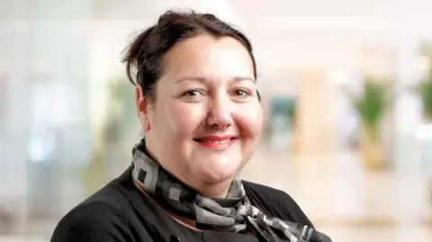 Thompsons Solicitors Amanda Jones is smiling at the camera. She is wearing a black top and a black/grey scarf. 