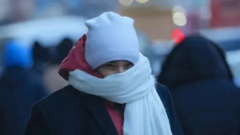 A woman bundles up in a hat, scarf and coat after the first snowfall in New York City on 23 December, 2023