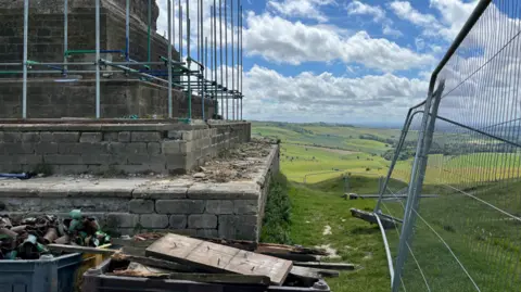 A grey metal fence in front of the foundations of a large stone monument