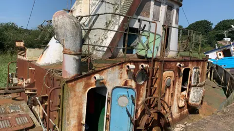 A rusted old boat in Annan harbour with doors open and a funnel showing
