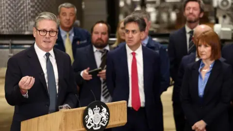 PA Media Sir Keir Starmer giving a speech next to the government podium with Rachel Reeves and Ed Miliband standing in the background