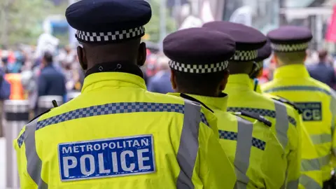 The backs of five Met Police officers, wearing hi-vis jackets with the name of the force on the back