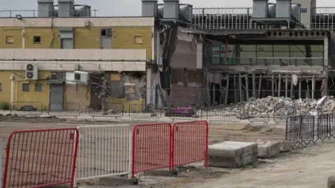 BBC Image shows Stretford Mall in the process of being demolished. It is a late 1960s building with much of one facade now removed and the interior exposed. 