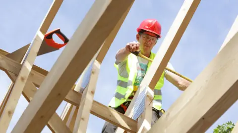Getty Images/Peter Cade Builder working on roof of house (stock photo)
