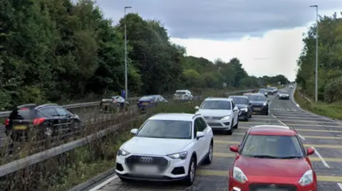 A Google Street View image of the road leading up to the Moor Farm Roundabout. It is a dual carriageway with metal barriers.