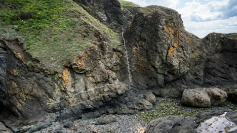 A rocky landscape in which a path is marked out with a chain attached to the rock face. The path includes a steep set of steps which cut through the rock.