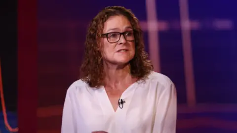 Getty A woman with curly hair and glasses wearing a white top speaking 
