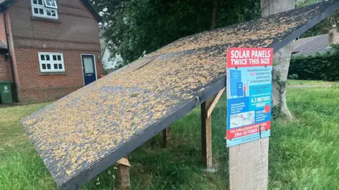 A board put up to depict a solar panel in a Cambridgeshire village with a sign next to it entitled 'Solar Panels Twice This Size'.