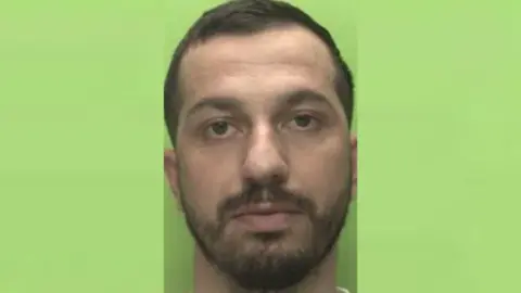 Nottinghamshire Police A headshot of Albjon Proi against a green background. He has a brown beard and short brown hair.