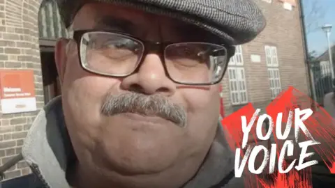 Anthony Lobo Close up photo of Anthony, a man in his 60s or 70s, standing in front of a brick building. The Royal Mail logo is faintly visible beside the building's entrance. BBC Your Voice branding is on the photo