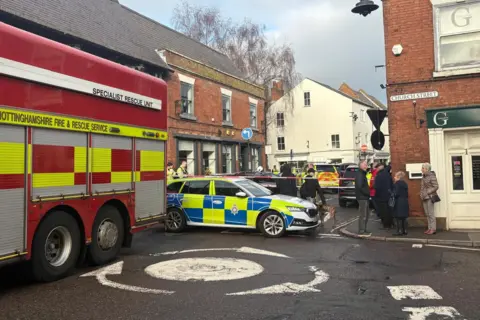 A fire engine and a police car in front of a cordon with people around it. 