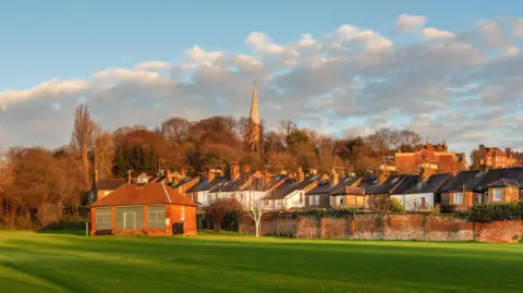 Getty Images Rows of 1930s houses on a slight hill with grassland in front and a church on a hill in the background. 