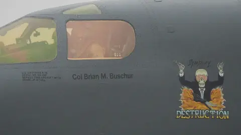 Getty Images A close-up image of a  B-1 Lancer cockpit, a painting on the side shows a skeleton in a suit jacket in an orchestra conducting pose. A text caption painted below reads: 'Symphony of Destruction'