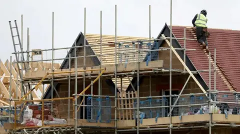 Houses being built with scaffolding and a builder laying tiles on a new roof