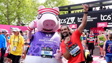 PA Media Joe Wicks, wearing his finisher's medal, poses for a photo with a person dressed in a large Daddy Pig mascot costume representing the National Deaf Children's Society.