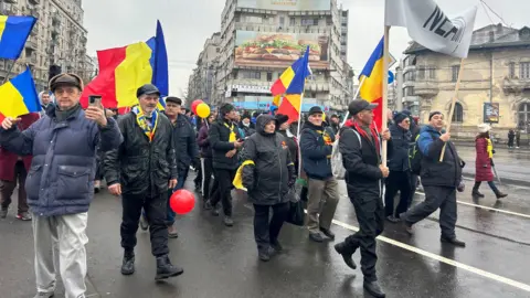 Crowds of people who marched Romanian flag through BBC Bucharest. Most are wearing dark clothes and hats.