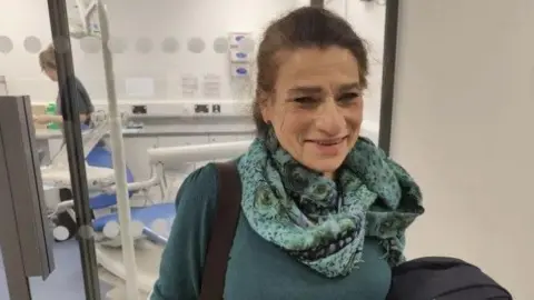 University of Plymouth Madga is wearing a blue jumper and scarf and smiling as she walks into the clinic