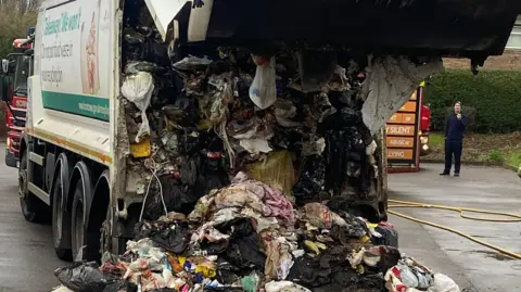 Broxtowe Borough Council Broxtowe Borough Council waste bin lorry has its back open with rubbish falling out and many rubbish bags are burned from the fire