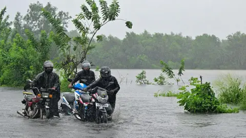 AFP via Getty Images Motorists wade through a flooded street in Biyagama on the outskirts of Colombo on 28 November 2025.
