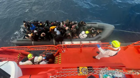 SALVAMENTO MARITIMO/REUTERS Spanish coast guards wearing white suits on a ship work on towing a rubber boat carrying migrants, including a newborn baby, off the island off the Canary Island of Lanzarote