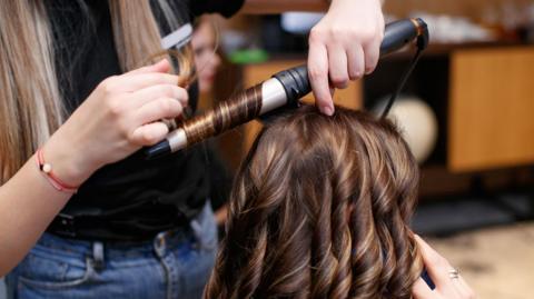 A young girl curling the hair of another girl