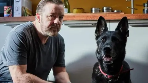 Ricky Gervais with an German shepherd dog in a room from his Netflix series After Life