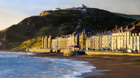 Getty Images An image of Aberystwyth promenade, with large seafront buildings above the beach, small waves lapping the shore and Constitution Hill in the background 