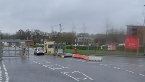 Road leading to check point with metal fencing around and red and white barriers either side of a hut in the centre of the road.