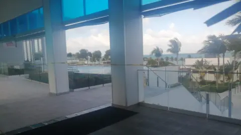 Colin Nulty View of the Riu Palace hotel reception looking out to the pools and palm trees with the sea in the background showing a yellow and black police crime scene tape.