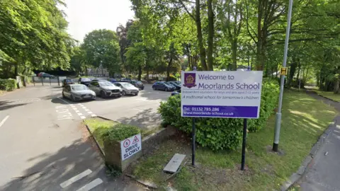 A white and purple sign outside a car park that reads: Welcome to Moorlands School