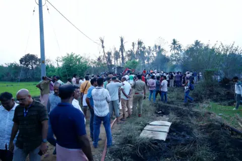 Arun Chandra Bose A group of men stand near a patch of blackened grass. A police officer can also be seen in the photo