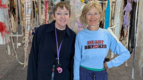Threads Textile Festival/The Marketing Tribe Two women smile widely surrounded by bits of yarn