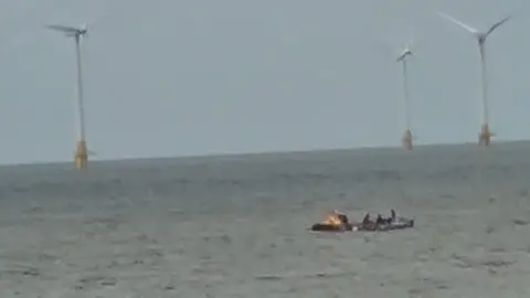 Old pictures / xa is taken by low-rupert and rewing crew out in the sea. In a distance there are three wind turbines. 