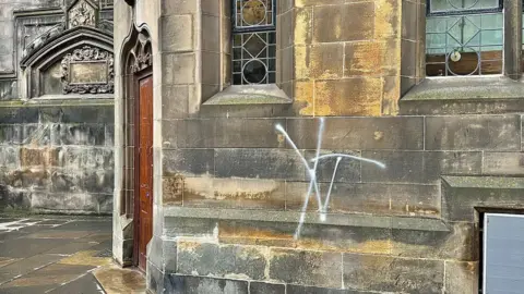 There is a white graffiti tag on the wall of the cathedral.