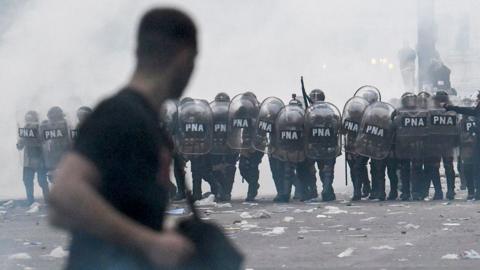 A protester is seen in the foreground with a line of police in the background with riot shields, tear gas all around them, in Buenos Aires on 12 June