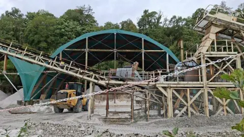 Caroline Martin/Geograph Industrial machinery, including a yellow tractor, surrounded by in-leaf trees