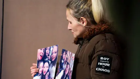 AFP via Getty Images Sarah Lampert shows two photos of her daughter Ticaria Lampert with her siblings. Her eyes are downcast, and she wears a brown winter coat