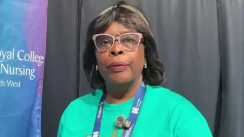 Beverley Nwosu has black straight hair and is wearing pink framed glasses, a green t-shirt and a blue lanyard which says Royal College of Nursing.
