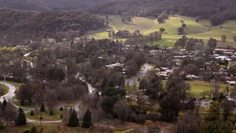 A birds-eye view shows the township of Porepunkah, a cluster of buildings and roads surrounded by green hills and dense bushland