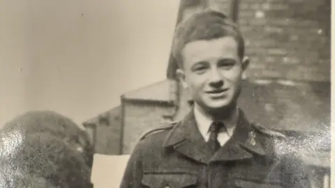 Handout Gordon Talbot is seen in a black and white photograph from the 1940s. He is wearing an RAF uniform. There is a row of houses behind him.