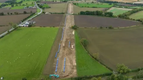 Overhead shot of green fields and blue pipes in a straight line 