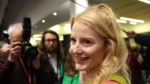 EPA Green Party candidate Hannah Spencer smiles as a photographer takes image and others crowd around