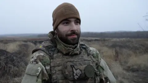 Denys stands outside wearing a military uniform 